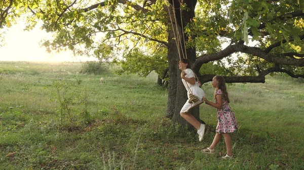 Kinderen die schommelen op een eiken tak in de zon. Dromen van vliegen. concept van een gelukkige jeugd. Mooie meisjes spelen in het park. tieners genieten van vliegen op swing op een zomeravond in het bos — Stockfoto