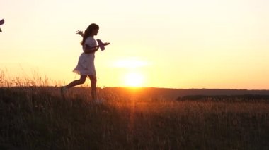 Uçma hayalleri. Mutlu çocukluk kavramı. Gün batımında iki kız bir oyuncak uçakla oynuyor. Güneşin arka planındaki çocuklar ellerinde bir uçakla. Uçakta oynayan çocukların silueti.