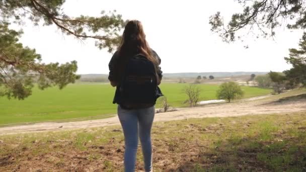 Mulher livre viajante com uma mochila sai da floresta e felizmente estende os braços para os lados, apreciando a natureza. menina saudável viaja medita ao ar livre. conceito de turismo — Vídeo de Stock