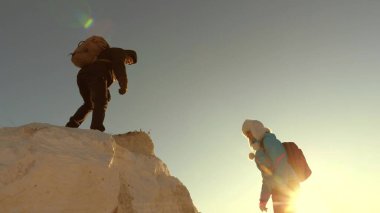 Erkek turist, gezgin bir kızın dağa tırmanmasına yardım eder, yardım elini uzatır. Özgür kadın dağlara el ele tırmanır. Gün batımında dağlarda seyahat ve macera. Turistlerin takım çalışması.