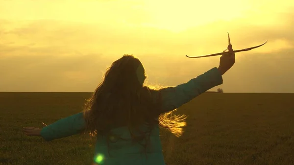 Barnet leker leksaksflygplan. Lycklig flicka springer med ett leksaksplan på ett fält i solnedgångens sken. Tonåringen drömmer om att flyga och bli pilot. Hon vill bli pilot och astronaut. Långsamma rörelser — Stockfoto