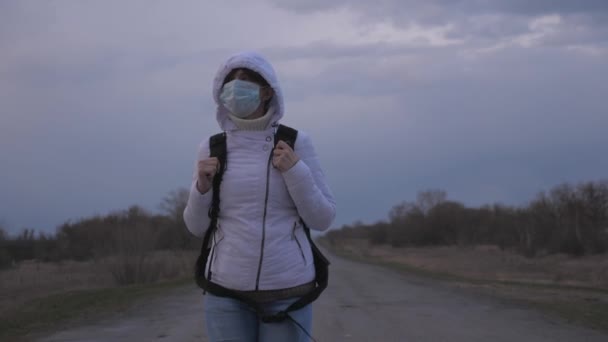 Viajero chica libre con una mochila en máscara médica protectora y capucha está caminando fuera de la ciudad en la carretera. Protección contra virus y bacterias. concepto de salud y seguridad, coronavirus N1H1, virus — Vídeo de stock