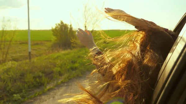 Free woman travels by car catches the wind with her hand from the car window. Girl with long hair is sitting in front seat of car, stretching her arm out window and catching glare of setting sun — Stock Photo, Image