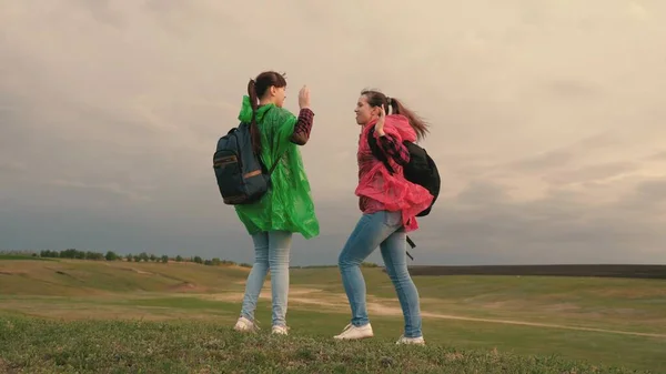 Donne sane turisti viaggiano con zaini in impermeabili colorati. Al rallentatore. lavoro di squadra dei viaggiatori. Ragazze-viaggiatori liberi andare ai margini della collina, gioire, applaudire le mani e saltare con felicità. — Foto Stock