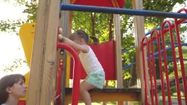 Anne ve bebek parkta oynuyorlar. Mutlu çocukluk kavramı. Mutlu çocukluk ve aile kavramı. Küçük çocuk gülüyor ve parktaki oyun alanının tadını çıkarıyor. Çocuk sokakta annesiyle oynuyor..