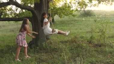 Çocuklar güneşin altında meşe dalında salıncakta sallanıyor. Uçma hayalleri. Mutlu çocukluk kavramı. Güzel kızlar parkta oynuyorlar. Genç kızlar ormanda bir yaz akşamı salıncakta sallanmaktan hoşlanırlar.