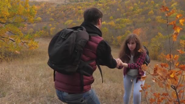 Teamwork of tourists. Climbers help a friend rise by holding out a helping hand to a friend. two tourists on top of the mountain. Travelers in the autumn on the hill admire the beautiful scenery — Stock Video