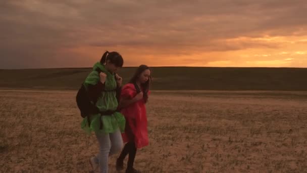 Gezonde toeristische meisjes reizen met rugzakken in kleurrijke regenjassen, storm nadert. vrije vrouwelijke reizigers gaan naar de kloof, hand in hand. teamwerk reizigers. Het concept van avontuur en reizen. — Stockvideo