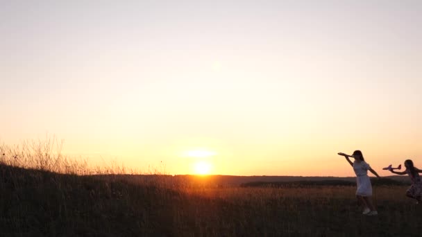 Drömmar om att flyga. Glad barndomsidé. Två flickor leker med ett leksaksplan vid solnedgången. Barn på bakgrunden av solen med ett flygplan i handen. Silhuett av barn som leker på planet — Stockvideo