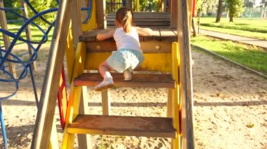 Çocuk merdivenlerden çıkıp çocuklar kayıyor. Anne ve bebek oyun bahçesinde oynuyorlar. Mutlu çocukluk kavramı. Mutlu çocukluk ve aile kavramı. Küçük çocuk gülüyor ve parkta oyun oynamaktan hoşlanıyor.