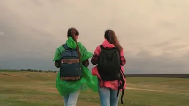 Sağlıklı kadın turistler renkli yağmurluklarla sırt çantalarıyla seyahat ederler. Ağır çekim. Gezginlerin takım çalışması. Özgür kızlar tepenin kenarına gider, sevinir, ellerini çırpar ve mutlulukla zıplarlar..