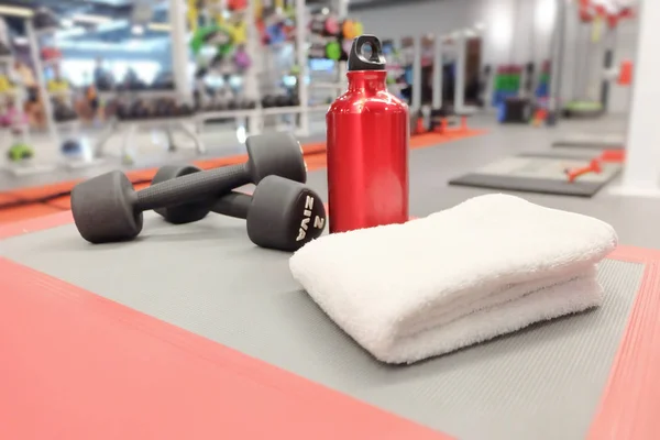 Sports equipment dumbbells, towel and bottle of red water in spo