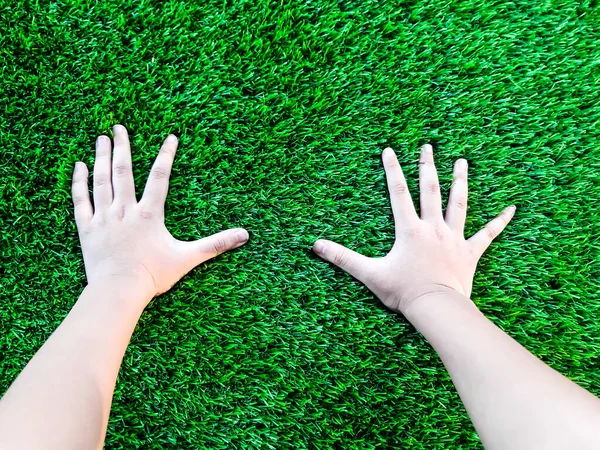 Yapay çim arka planı. Yeşil bir yapay çim zemininde bir çocuğun eli. Çocuk oyunu eğlencelidir..