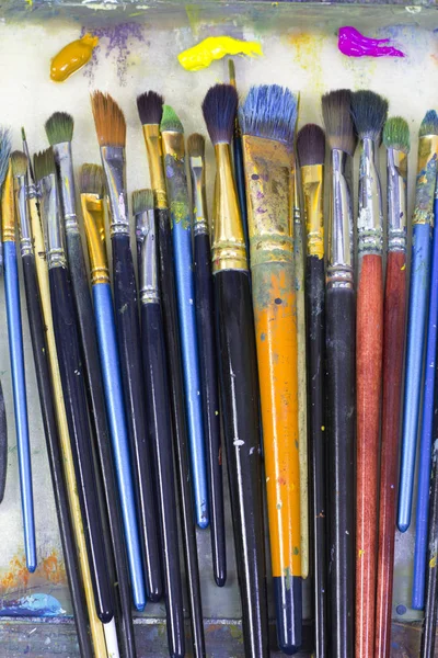 many art brushes lie on the palette, colored paints