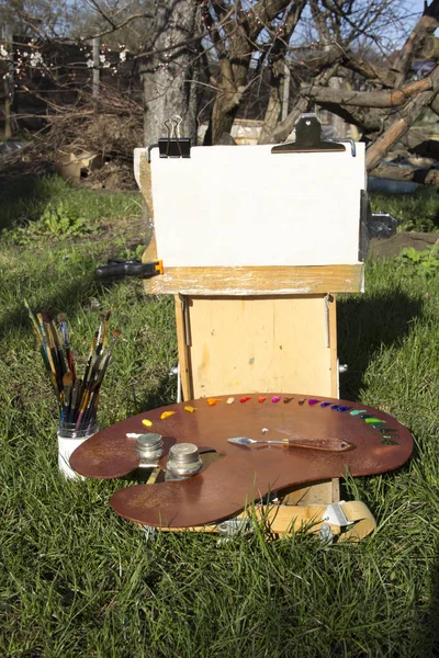 Plein air Etude Sketchbook for paintings. A palette with multicolored paints and palette knife lies on palette. White canvas for text, image. Plenary, creativity, hobby, inspiration, harmony.
