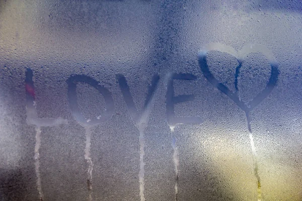 Rainy weather, the inscription love and hand-drawn heart on the sweaty glass.