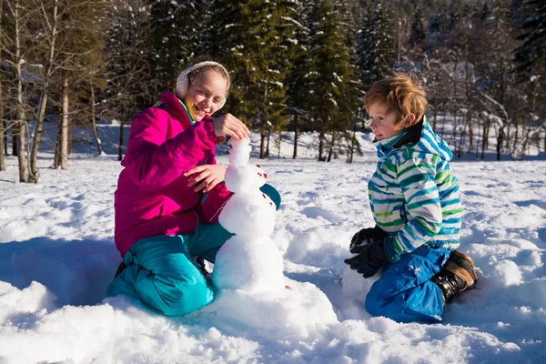 Siblings Building Snowman Together Sunny Day – stockfoto