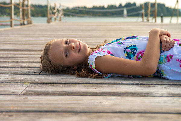 School girl lies on pier at sunset during holidays
