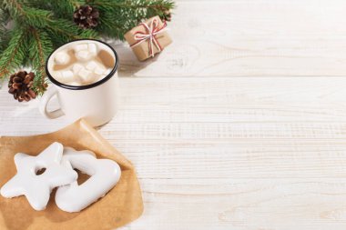 Hot Christmas drink with marshmallows in an iron mug and gingerbread cookies, on a white table. New Year, holiday background, copy space.