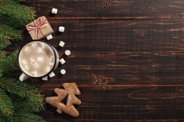 Hot Christmas drink with marshmallows in iron mug and gingerbread cookies, on a wooden table. New Year, holiday background, greeting card copy space.
