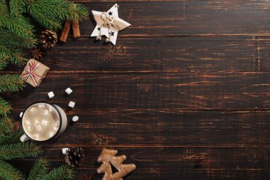 Hot Christmas drink with marshmallows in iron mug and gingerbread cookies, on a wooden table. New Year, holiday background, greeting card copy space.