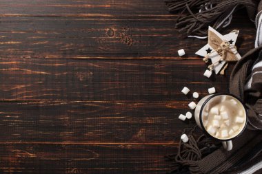 Hot Christmas drink with marshmallows in an iron mug, on a wooden table and a scarf. New Year, holiday background, greeting card copy space.