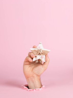 A male hand sticks out of a hole in pink paper, holds a Christmas tree ornament. Christmas concept symbol, commercial bucket print, copy space.