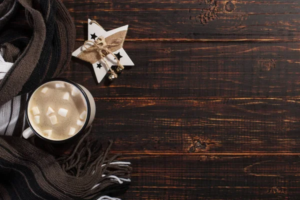 Bebida caliente de Navidad con malvaviscos en una taza de hierro, sobre una mesa de madera y una bufanda. Año Nuevo, fondo de vacaciones, espacio de copia de la tarjeta de felicitación . — Foto de Stock