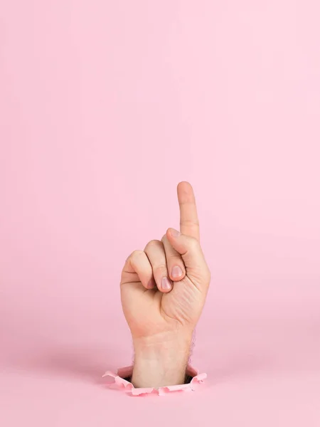 Männliche Hand ragt aus einem Loch in Papier, auf rosa Hintergrund. zeigt ein Zeichen an, Leerzeichen kopieren. — Stockfoto