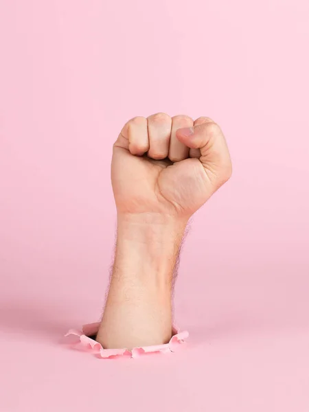 Männliche Hand ragt aus einem Loch in Papier, auf rosa Hintergrund. zeigt ein Faustzeichen an, Kopierraum. — Stockfoto