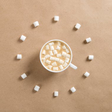 Kahverengi el işi kağıdında krema olan beyaz bir fincan kahve, saat şeklinde şekerlemeler..