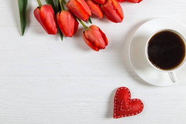 Beyaz masada kırmızı laleler, kalp ve bir fincan kahve. Bahar tatili için sabah hediyesi, Anneler Günü. Boşluğu kopyala.
