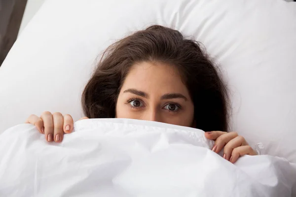 Young pretty woman hiding under blanket lying on bed — Stock Photo, Image