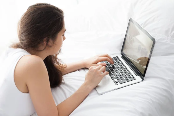 Красивая женщина лежит на белой кровати с помощью ноутбука — стоковое фото