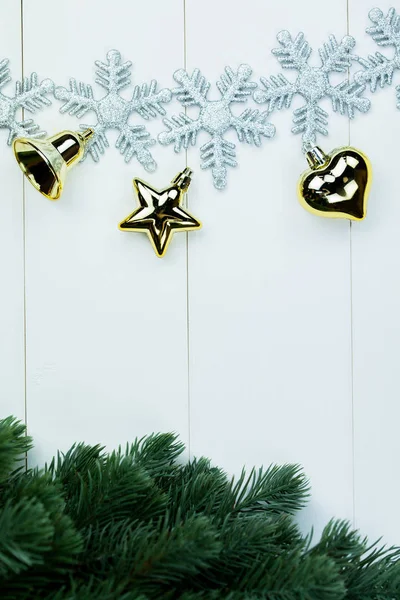 Part of spruce Christmas tree and golden ornaments and snowflakes on white wood background. — Stock Photo, Image