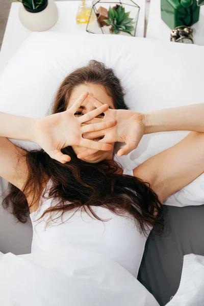 Beautiful young Caucasian smiling woman covering her eyes on bed — Stock Photo, Image