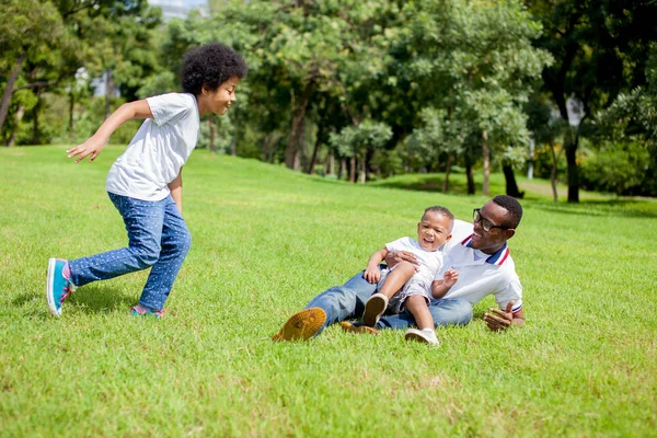 Two kids chasing and playing together while dad caught a boy in park. — Stock Photo, Image
