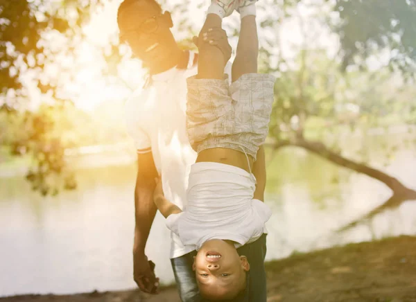 Papá sosteniendo a un hijo boca abajo en el parque bajo la luz del sol — Foto de Stock