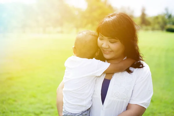 Азиатская мать, несущая и держащая сына в солнечном свете в зеленом парке — стоковое фото