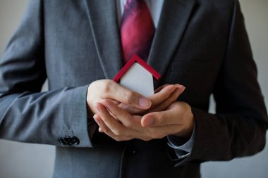 İş adamı kapsayan ve ev - koruma ellerini iş mortgage, Emlak kredi, ev sigortası, iş yatırım kavramı kullanarak takım elbiseli.