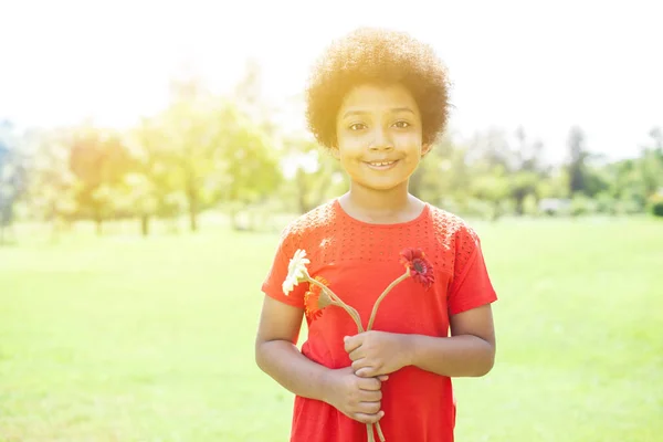 Chica afroamericana sonriente feliz sosteniendo flores en el parque — Foto de Stock