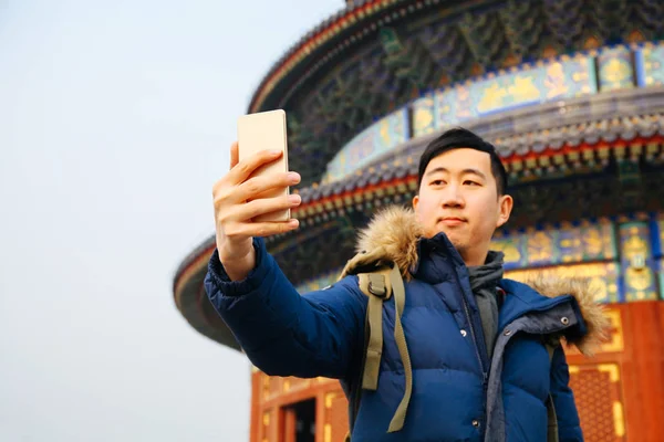 男性冬のジャケットを着て、中国の寺院の背景 (セレクティブ フォーカスの上のスマート フォンを使用して) — ストック写真