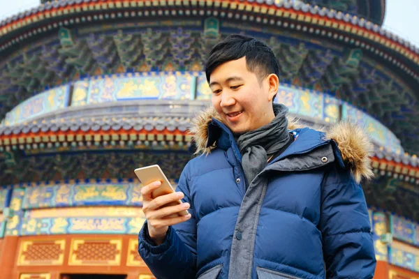 Hombre asiático con chaqueta de invierno y el uso de un teléfono inteligente sobre fondo templo chino (enfoque selectivo ) — Foto de Stock