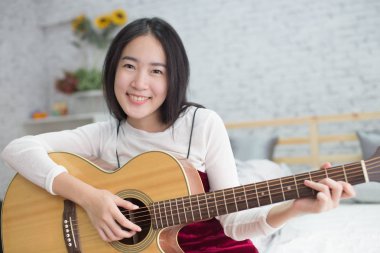Yatak odasında akustik gitar çalmak mutlu ve sevimli gülümseyen Asyalı kız