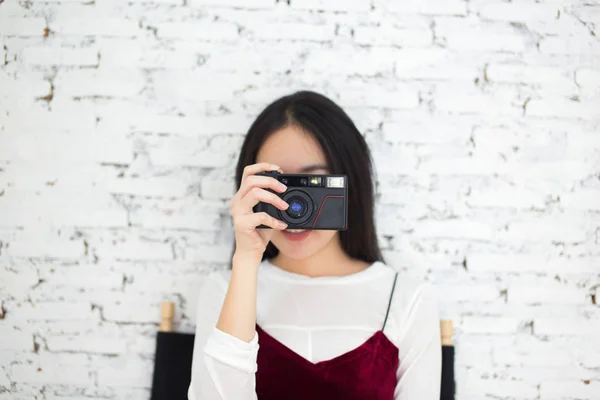 Asian woman pointing a retro camera in front in vintage wall