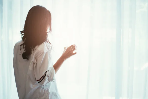 Woman holding a glass of water while looking out of the window - back of silhouette woman — Stock Photo, Image