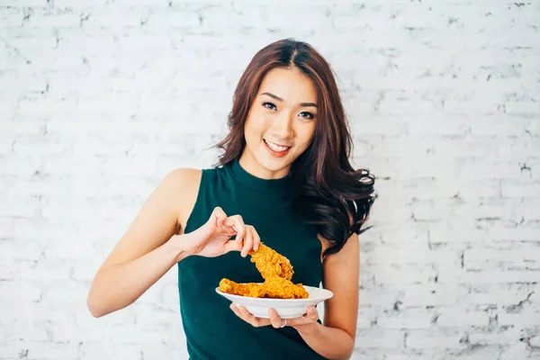 Attraktiva asiatisk kvinna äta stekt kyckling kycklingben över vitt tegel bakgrund — Stockfoto