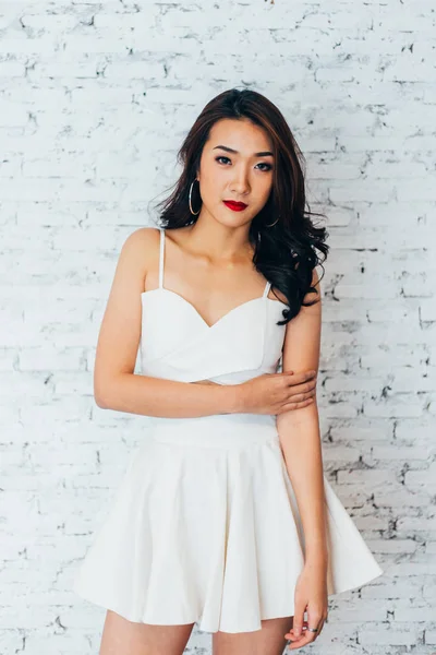 Jeune femme asiatique posant en robe à la mode sur mur de briques blanches — Photo