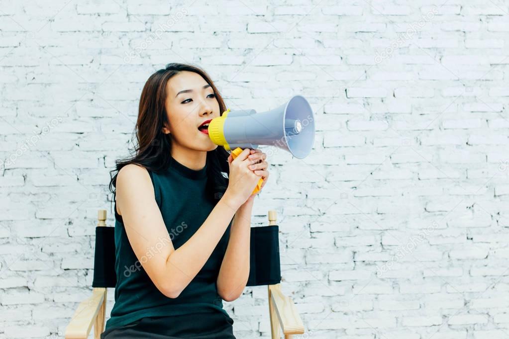 Asian business woman shouting with megaphone over white bricks wall background