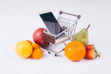 Mobil ticaret ve e-ticaret bakkal için gösteren çeşitli meyve ve yiyecek içinde smartphone ile dolu bir alışveriş sepeti